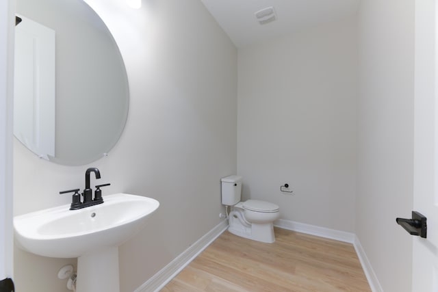 half bath featuring visible vents, baseboards, toilet, wood finished floors, and a sink