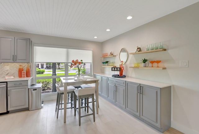 kitchen with light countertops, stainless steel dishwasher, backsplash, gray cabinets, and open shelves