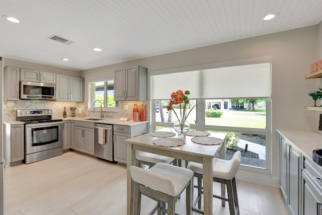 kitchen with decorative backsplash, gray cabinetry, appliances with stainless steel finishes, light wood-style floors, and a sink