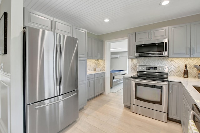 kitchen featuring light stone counters, appliances with stainless steel finishes, light wood-type flooring, backsplash, and gray cabinets