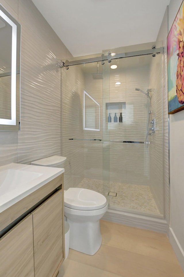 full bathroom with a stall shower, tile walls, vanity, and toilet