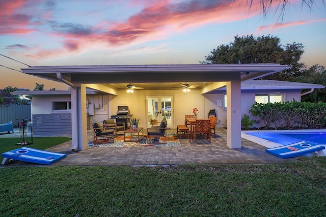 back of house at dusk with a patio, a ceiling fan, a yard, a fenced in pool, and stucco siding