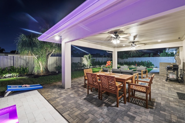 patio at night featuring a fenced backyard, a ceiling fan, and outdoor dining space