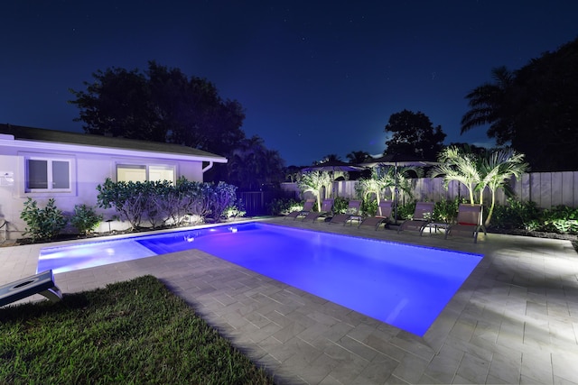 pool at night with a patio area, a fenced backyard, and a fenced in pool