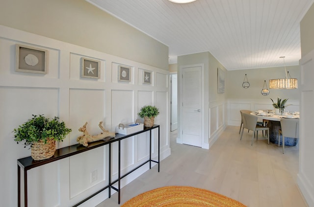 corridor with light wood-style floors, wood ceiling, and a decorative wall