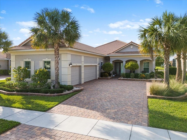 mediterranean / spanish-style house featuring a tiled roof, decorative driveway, an attached garage, and stucco siding