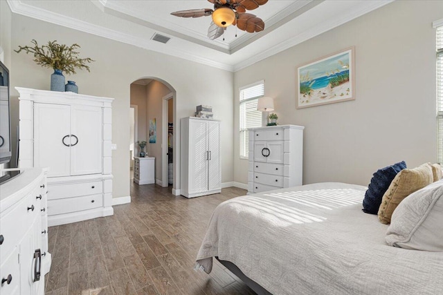 bedroom with visible vents, arched walkways, wood finished floors, a tray ceiling, and crown molding