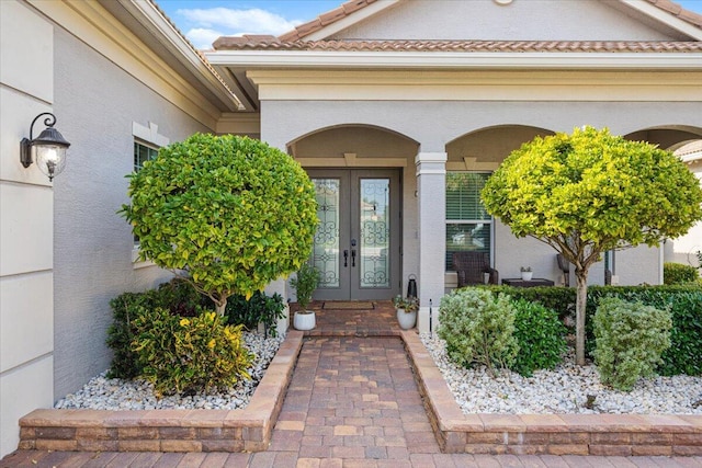 view of exterior entry featuring french doors, a tiled roof, and stucco siding