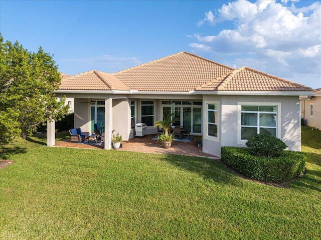 rear view of house featuring a patio area, a yard, a tiled roof, and stucco siding