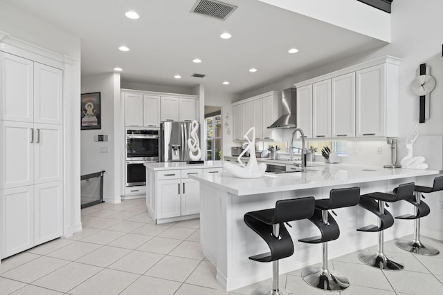 kitchen featuring light tile patterned floors, stainless steel appliances, a peninsula, visible vents, and wall chimney range hood