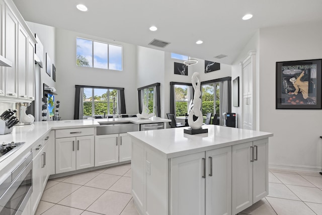 kitchen with light tile patterned flooring, a peninsula, a sink, visible vents, and a center island