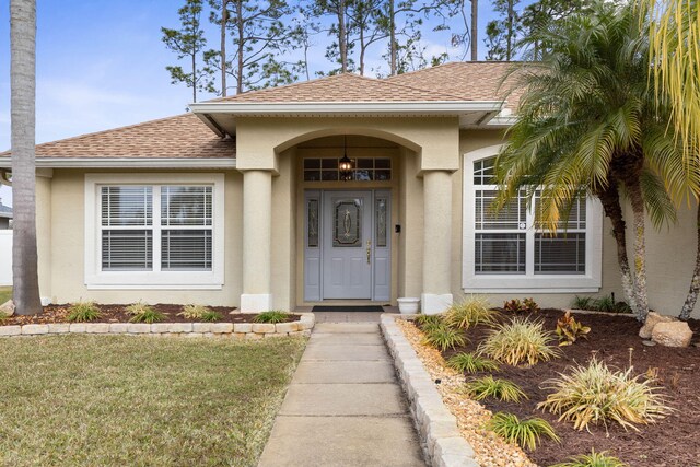 property entrance featuring stucco siding, a yard, and roof with shingles