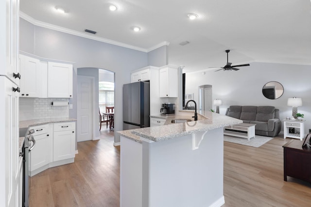 kitchen with arched walkways, a sink, white cabinets, open floor plan, and freestanding refrigerator