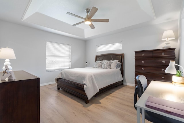 bedroom featuring baseboards, a tray ceiling, a ceiling fan, and light wood-style floors