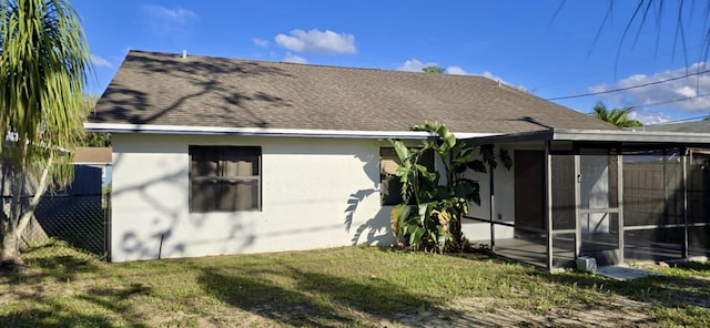 rear view of property with a sunroom, a shingled roof, a lawn, and stucco siding