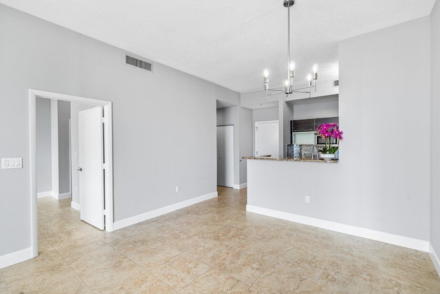 unfurnished living room featuring baseboards, a textured ceiling, visible vents, and an inviting chandelier