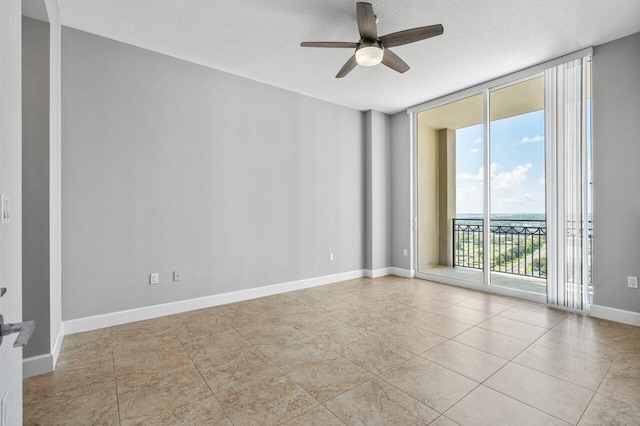 empty room with light tile patterned floors, baseboards, ceiling fan, a wall of windows, and a textured ceiling