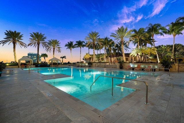 pool at dusk featuring a gazebo, a patio area, and a community pool