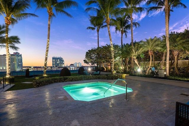 pool at dusk featuring a patio area, a view of city, fence, and a community hot tub