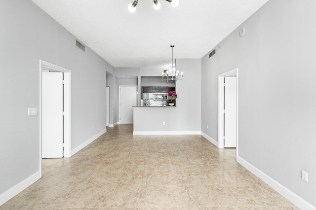 unfurnished living room with visible vents, a notable chandelier, and baseboards