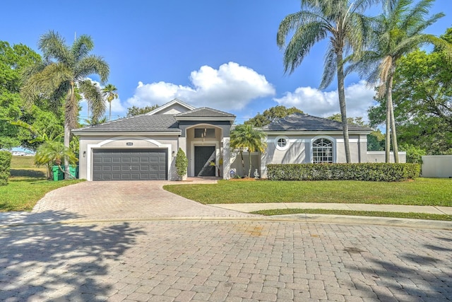 mediterranean / spanish house featuring stucco siding, decorative driveway, fence, a front yard, and a garage