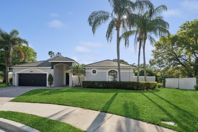 mediterranean / spanish home with stucco siding, decorative driveway, fence, a front yard, and an attached garage