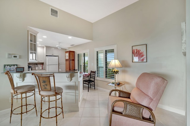 kitchen with a breakfast bar, visible vents, glass insert cabinets, freestanding refrigerator, and a peninsula