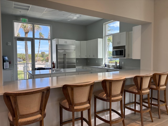 kitchen featuring light countertops, appliances with stainless steel finishes, white cabinets, a sink, and a peninsula