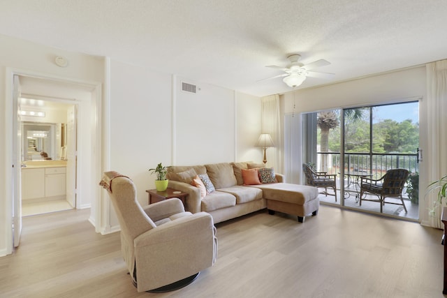 living room with light wood finished floors, ceiling fan, visible vents, and a textured ceiling