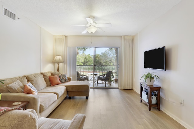 living room featuring visible vents, baseboards, ceiling fan, a textured ceiling, and light wood-style floors