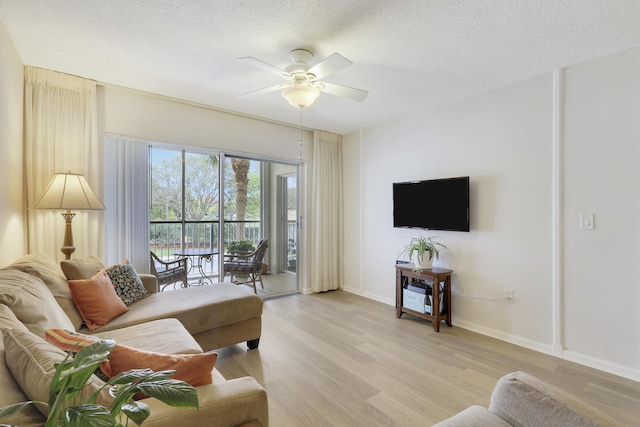 living area featuring light wood finished floors, baseboards, a ceiling fan, and a textured ceiling