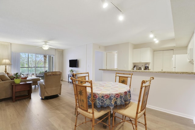 dining room with light wood finished floors, rail lighting, baseboards, and a ceiling fan