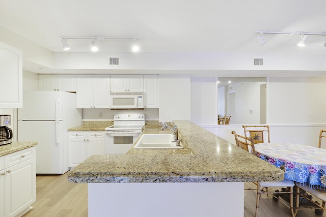 kitchen with visible vents, a sink, light wood-type flooring, white appliances, and a peninsula