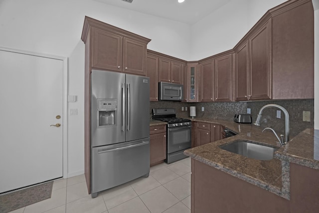 kitchen with a sink, appliances with stainless steel finishes, decorative backsplash, dark stone counters, and glass insert cabinets