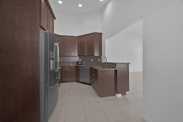 kitchen featuring decorative backsplash, a peninsula, light stone countertops, stainless steel appliances, and a sink