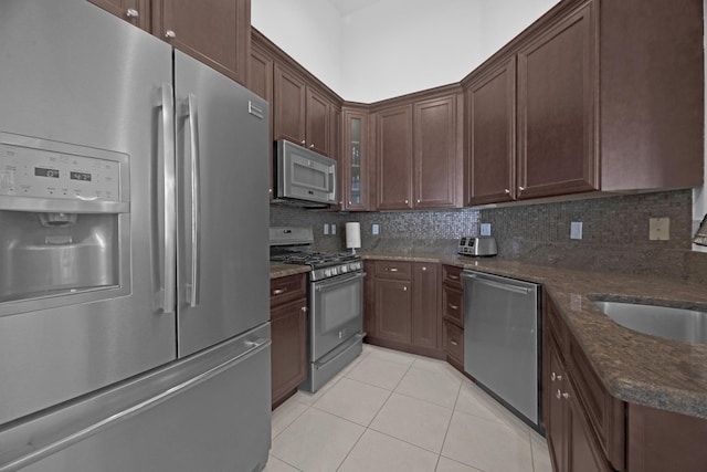 kitchen with light tile patterned floors, appliances with stainless steel finishes, glass insert cabinets, and decorative backsplash