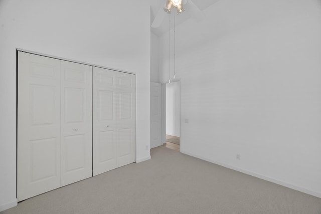 unfurnished bedroom with a closet, a high ceiling, a ceiling fan, carpet flooring, and baseboards