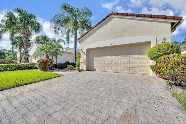 mediterranean / spanish-style house with an attached garage, stucco siding, decorative driveway, and a front yard