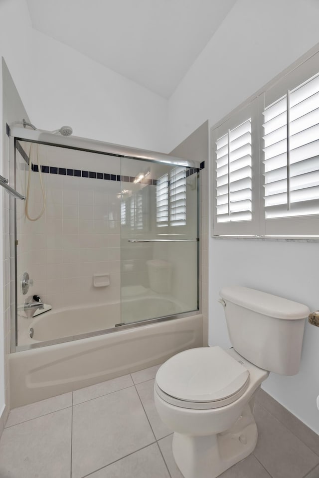 bathroom featuring tile patterned flooring, combined bath / shower with glass door, and toilet