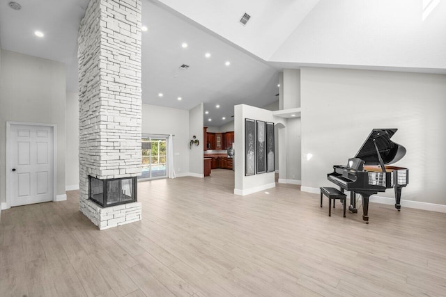 living area with high vaulted ceiling, a stone fireplace, light wood-type flooring, and visible vents