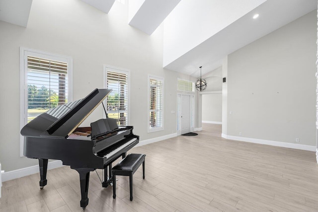 sitting room with high vaulted ceiling, baseboards, light wood finished floors, and an inviting chandelier