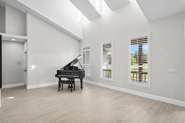 living area with high vaulted ceiling, light wood-type flooring, a skylight, and baseboards