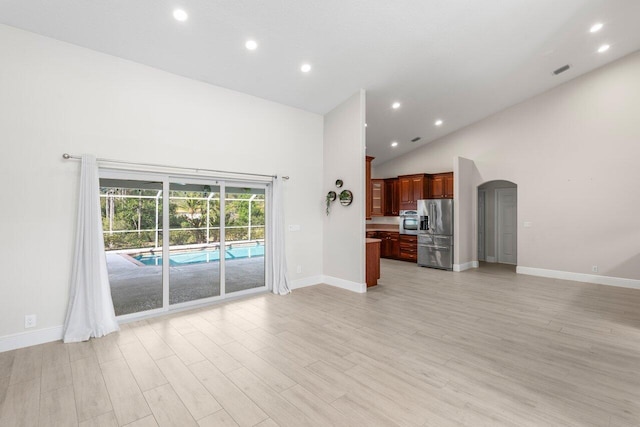 unfurnished living room with arched walkways, light wood finished floors, visible vents, high vaulted ceiling, and baseboards