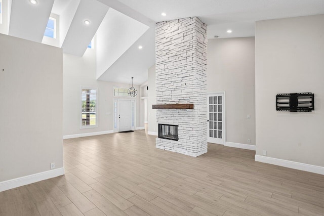 unfurnished living room with light wood finished floors, baseboards, a fireplace, high vaulted ceiling, and recessed lighting