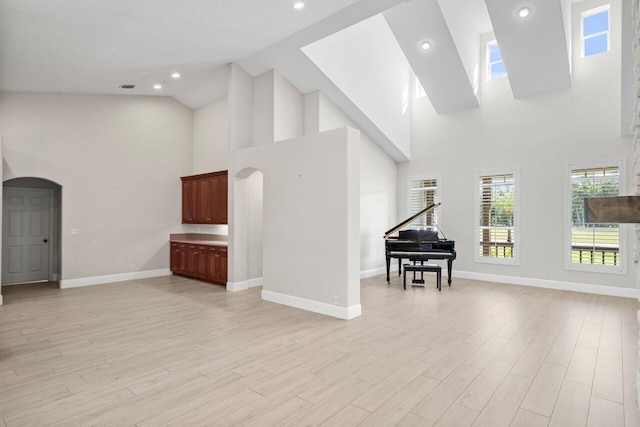 living area with arched walkways, light wood-style flooring, and baseboards