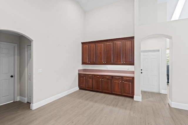 bar featuring light wood-type flooring, high vaulted ceiling, baseboards, and arched walkways