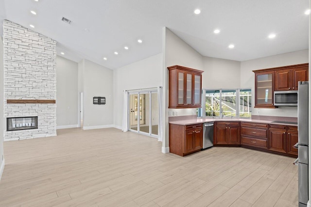 kitchen with a stone fireplace, light wood-style flooring, stainless steel appliances, light countertops, and glass insert cabinets