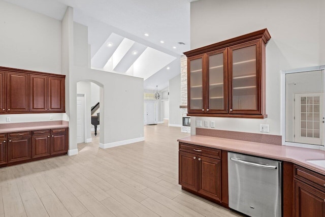 kitchen featuring arched walkways, light countertops, stainless steel dishwasher, glass insert cabinets, and light wood-style floors