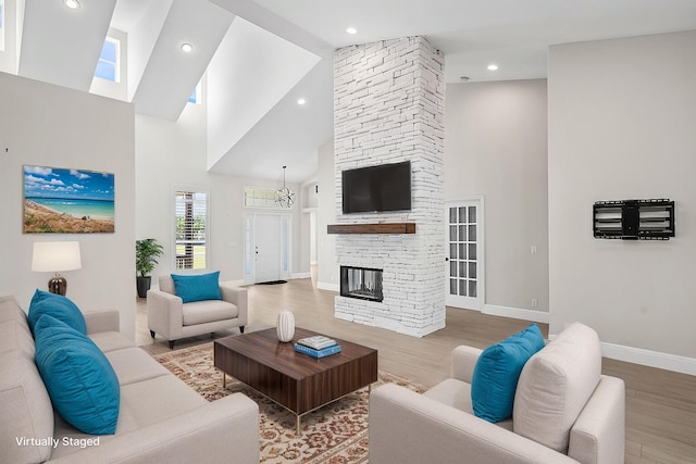 living area with high vaulted ceiling, a stone fireplace, baseboards, and wood finished floors