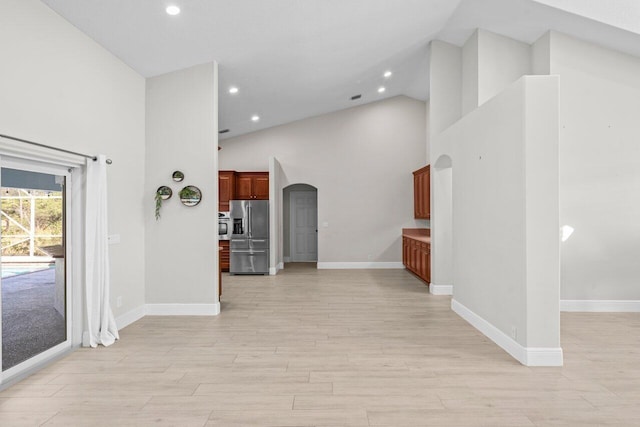 interior space featuring light wood finished floors, baseboards, arched walkways, high vaulted ceiling, and recessed lighting